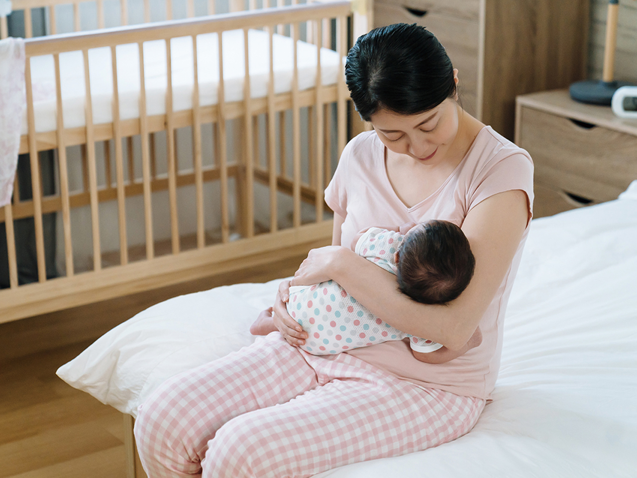 asian female sitting at bedside holding her baby that just fell asleep. portrait of mother looking and loving her child dearly